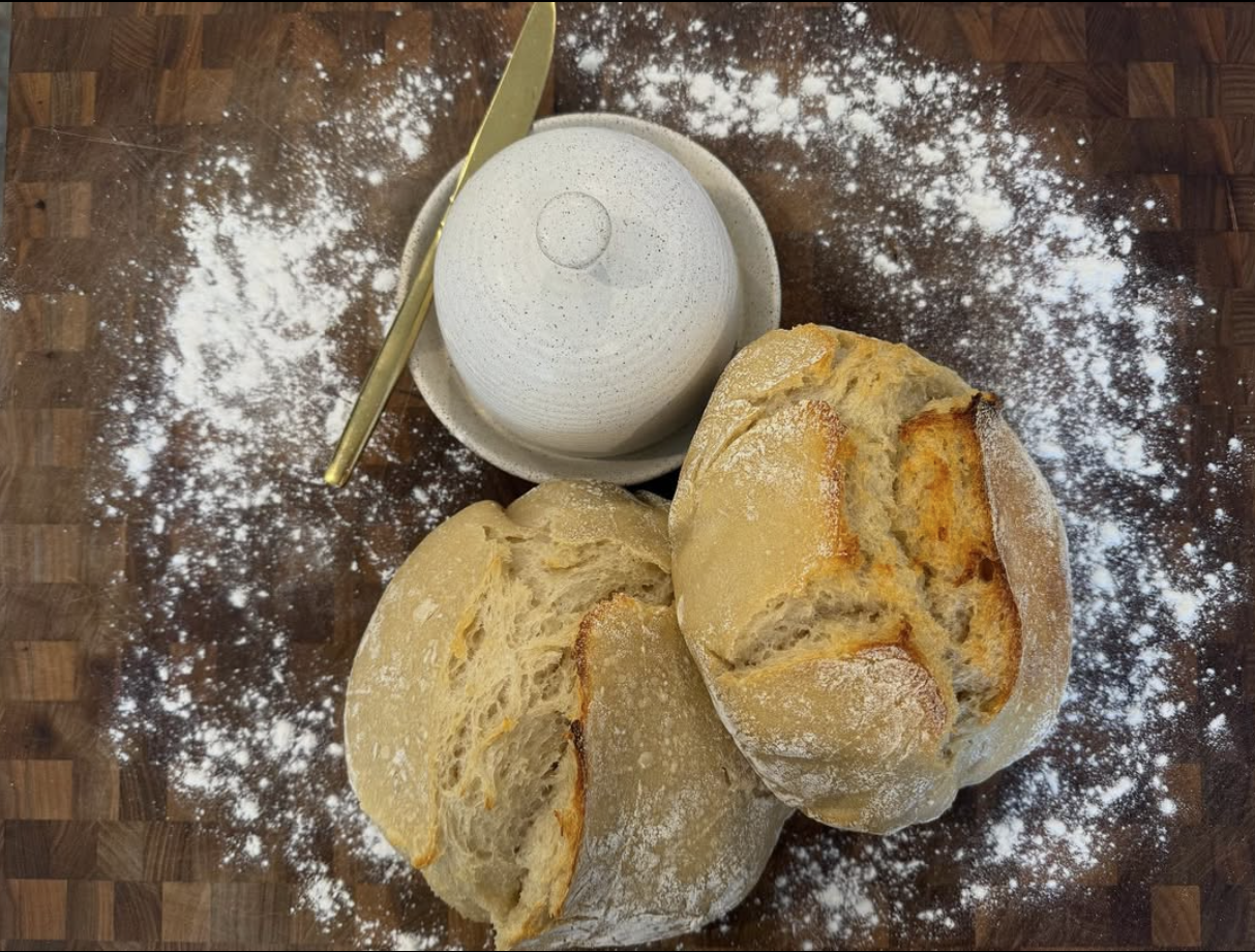 Two of Kara’s fresh sourdough loaves on a flour-dusted butcher-block counter